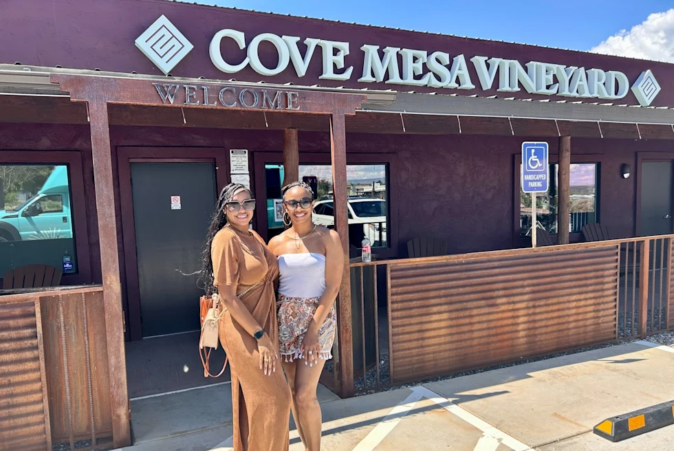 two woman outside a building with a sign that reads, cove mesa vineyard"