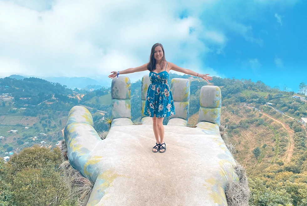 girl in blue flower dress standing on top of large white hand statue in Guatemala