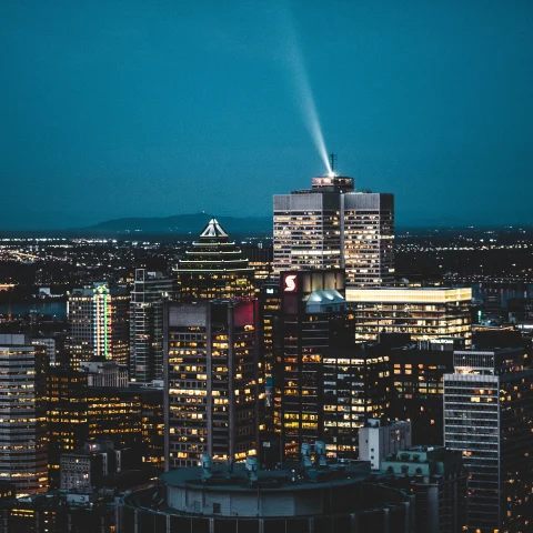 a city view of Montreal at night with dark blue skies and shiny tall gray buildings with yellow lights