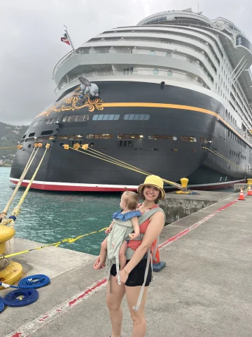 Travel advisor and baby posing before the Disney Cruise Ship at port on a cloudy day.