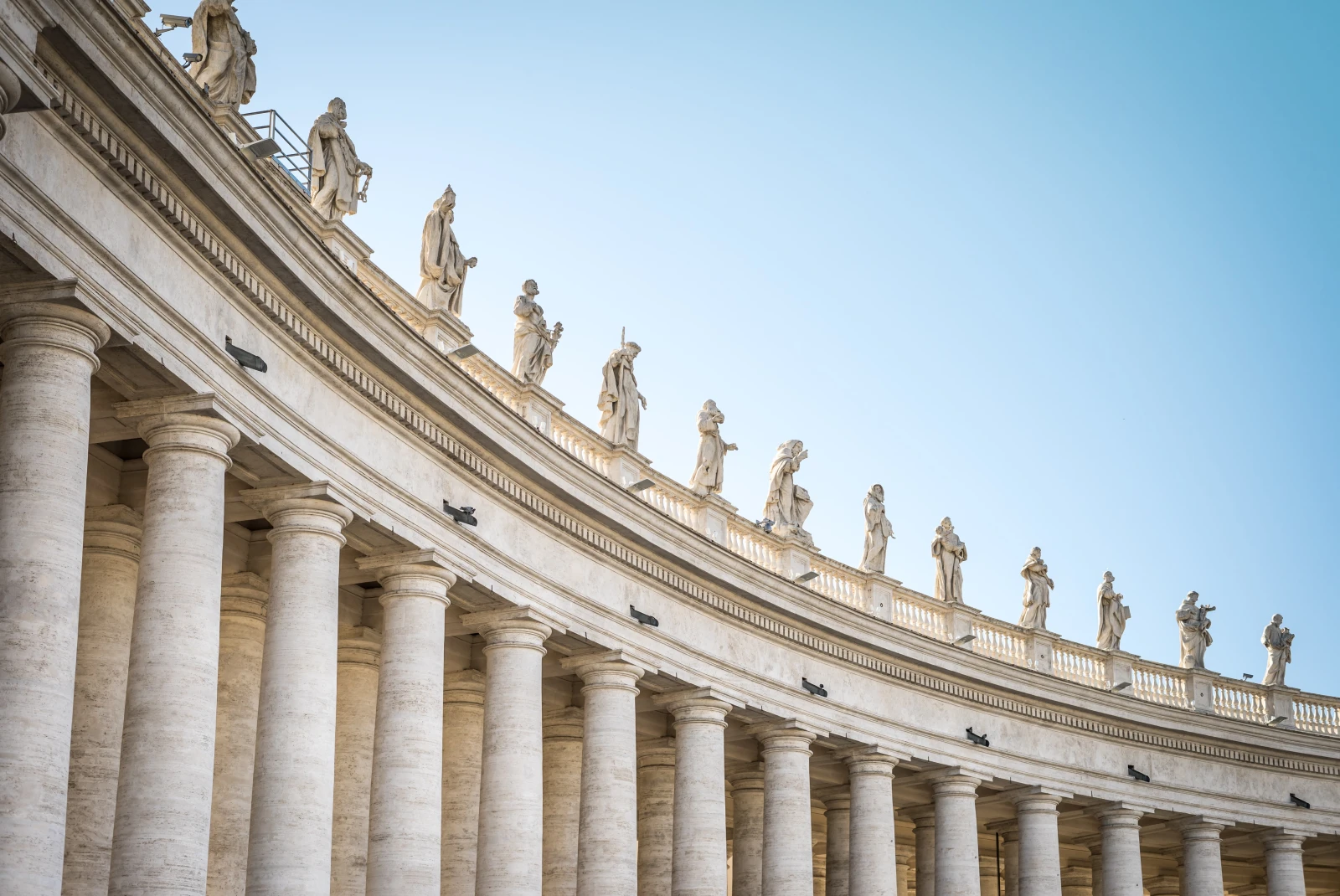 White statues and columns against a blue sky at the Vatican City in Italy.