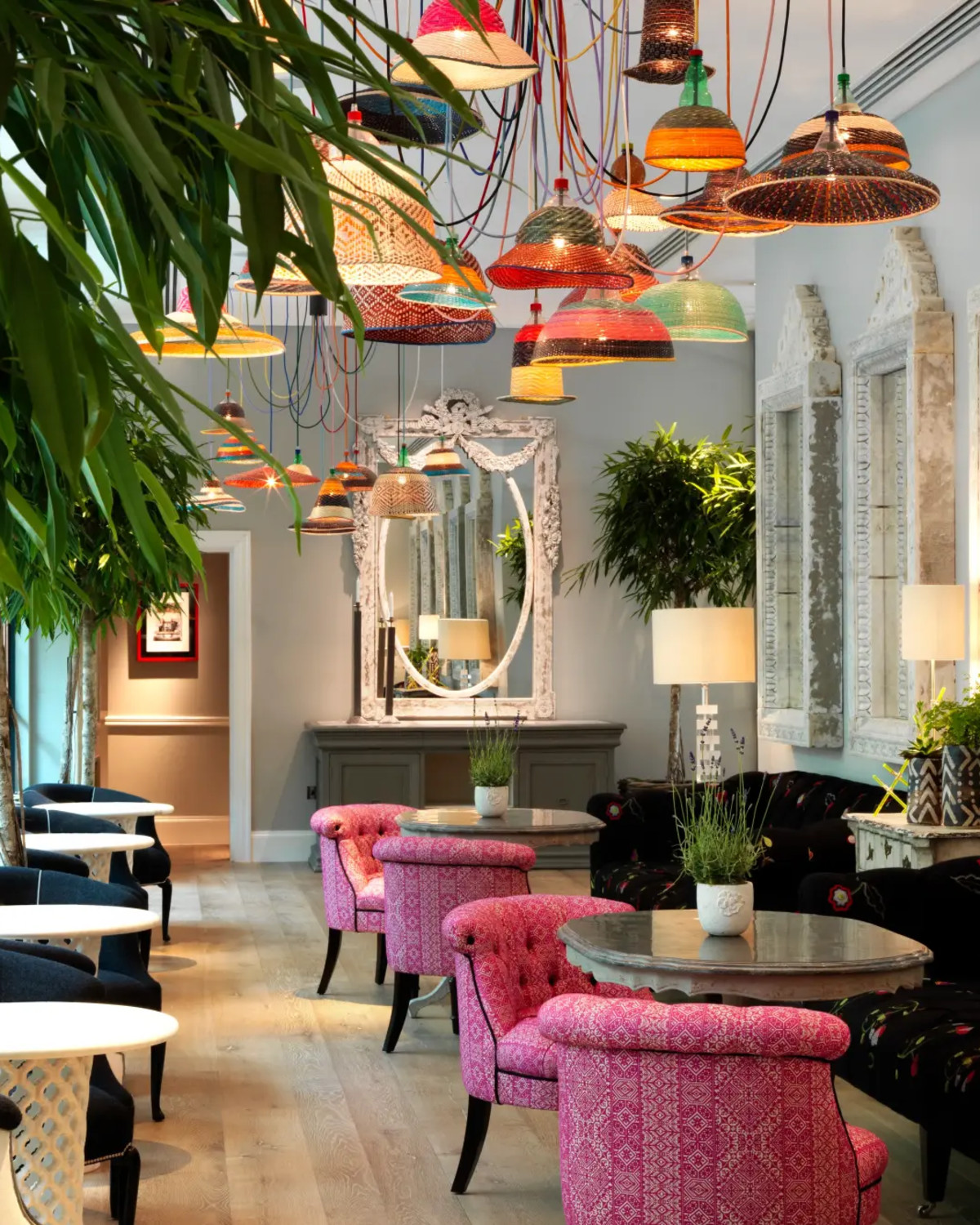 a colorful dining room with woven light fixtures and plants and pink chairs