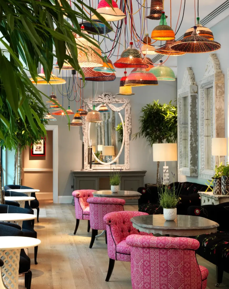 a colorful dining room with woven light fixtures and plants and pink chairs