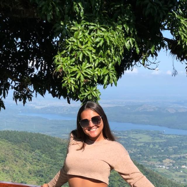Fora Travel Agent Kelsey Pina wearing tan shirt and sunglasses with green hills and river in the background