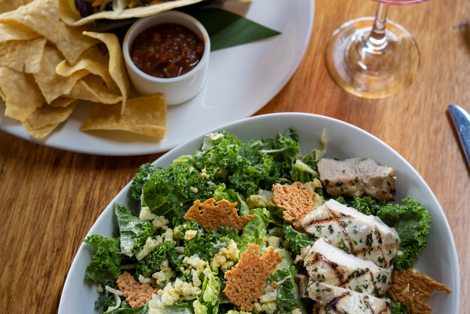 Fish tacos and a green kale salad on white plates with a pink cocktail at Leilani's On The Beach in Maui, Hawaii.