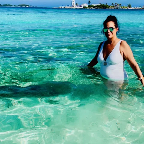 Jennifer waist-deep in the clear, turquoise waters of the Bahamas, with the coastline in the background. 