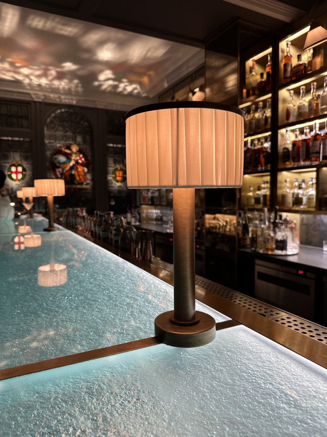 A close-up view of a lit table lamp on the bar at Donovan Bar with shelves of bottles in the background