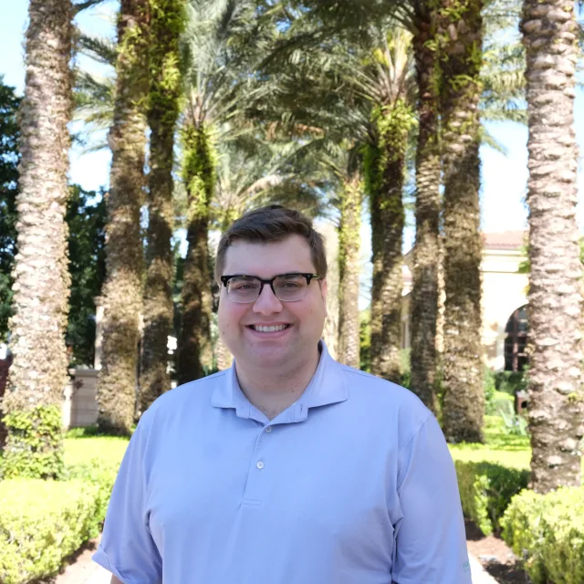 Travel Advisor Tom Grojean in a blue shirt in front of a line of palm trees.