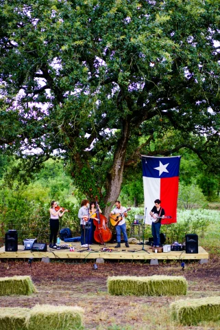 Field and stage with band playing with Texas flag and tree in background