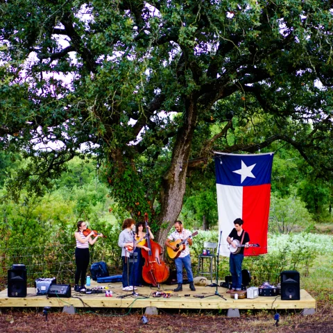 Field and stage with band playing with Texas flag and tree in background