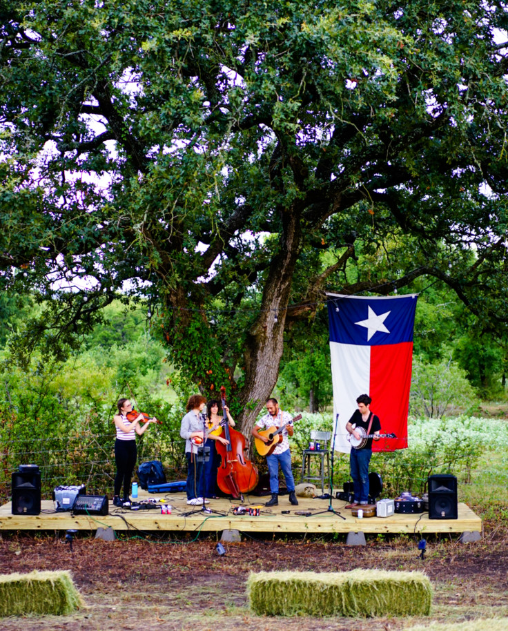 Field and stage with band playing with Texas flag and tree in background