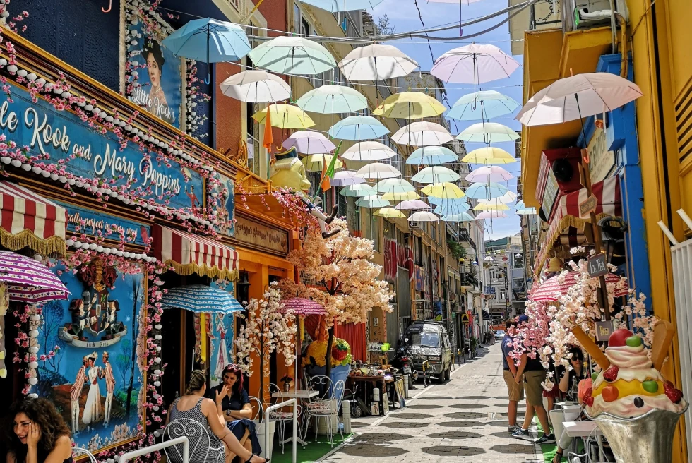 A narrow street with colorful cafes and umbrellas. 