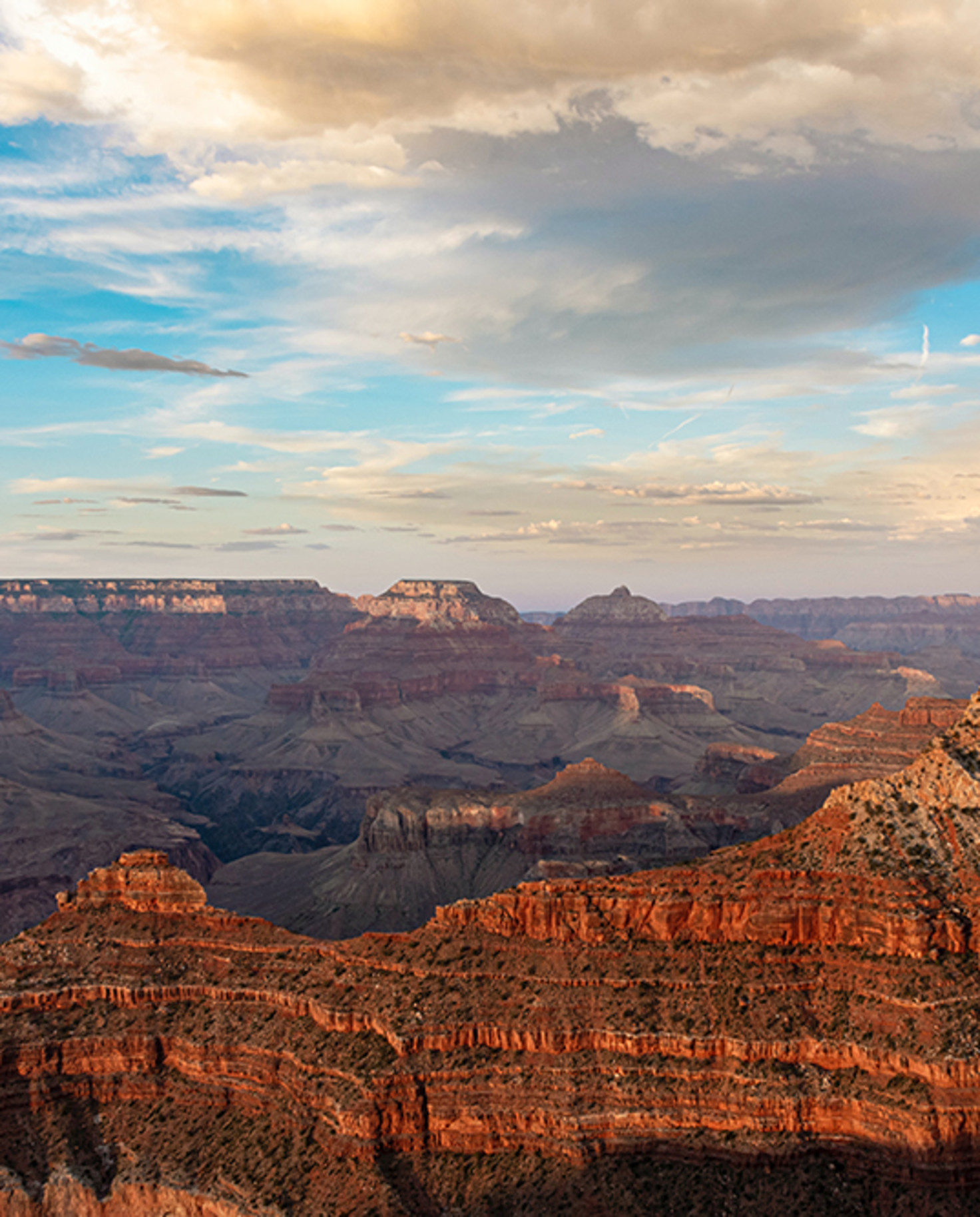 grand canyon in Arizona at sunset with red and tan ridges blue sky and white yellow clouds