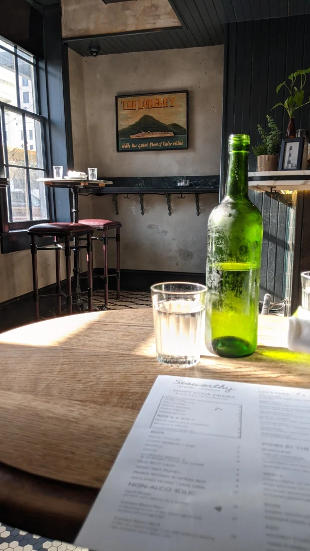 A glass of water and a green bottle on a wooden table