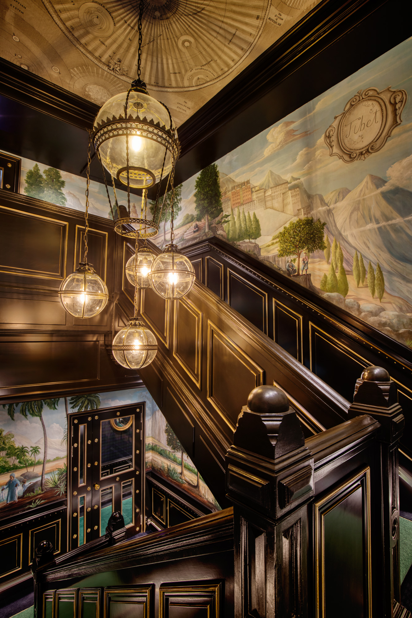 a handsome staircase in a building with colorful wallpaper and hanging globe lights