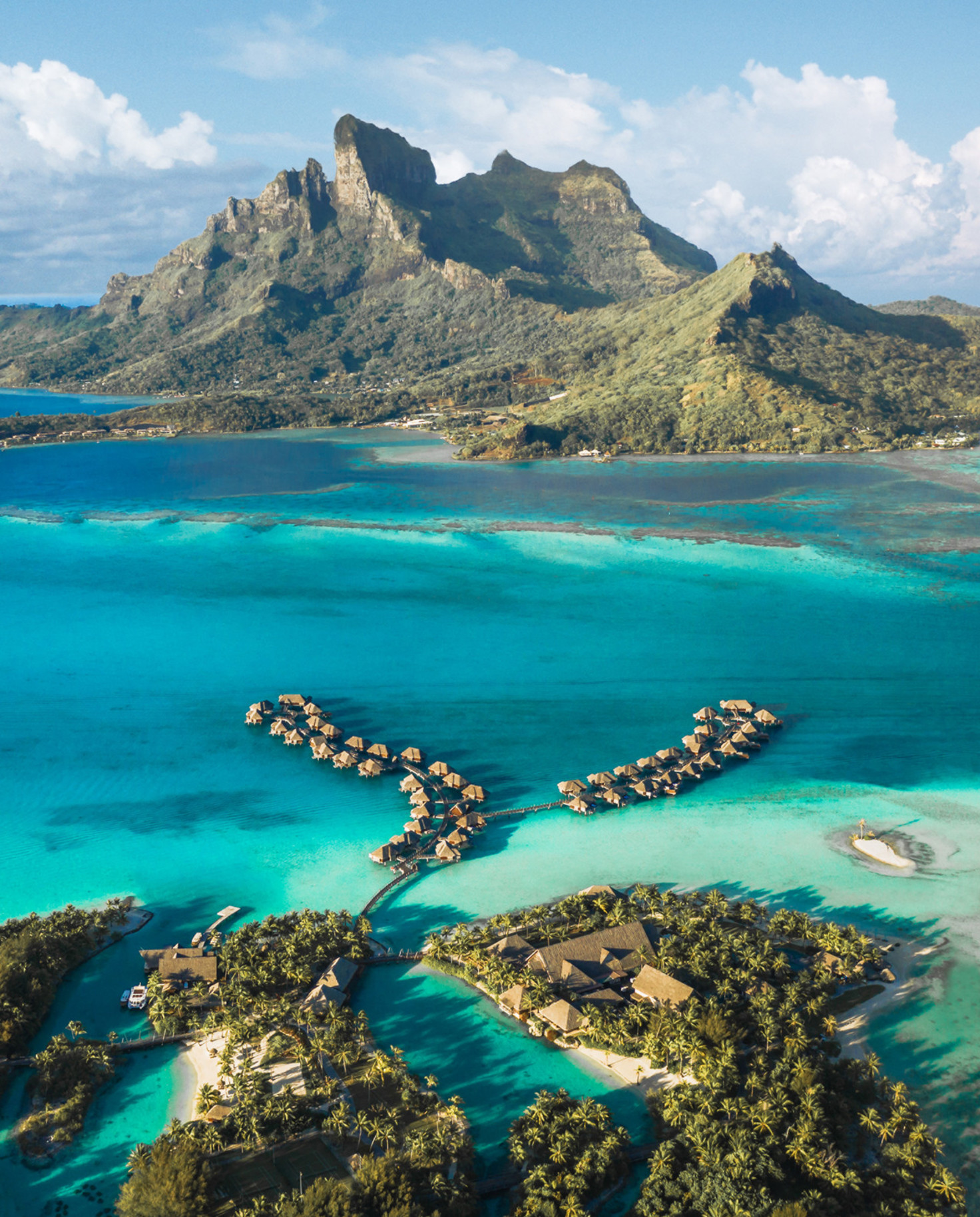 aerial view of bungalows in water with mountains in the background