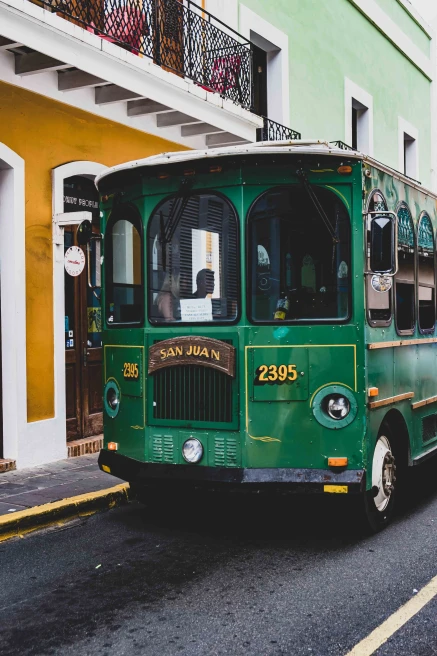 Green bus on the street next to a yellow building during daytime