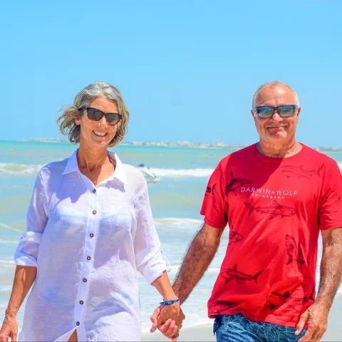 A man and woman walking on a beach holding hands.