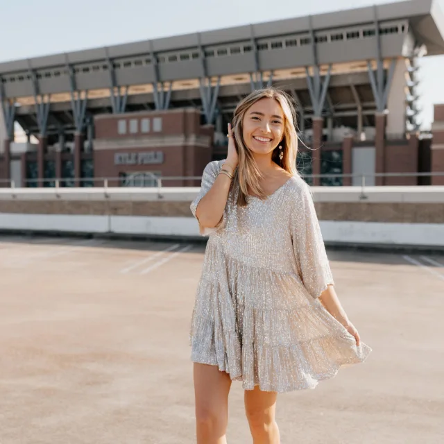 Travel Advisor Allana Webb wears a flowy white dress standing in front of a sports stadium