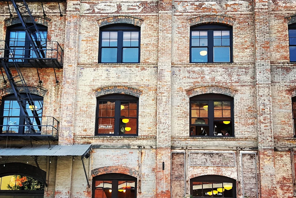 facade of a light brick building with fire escape and lit up windows