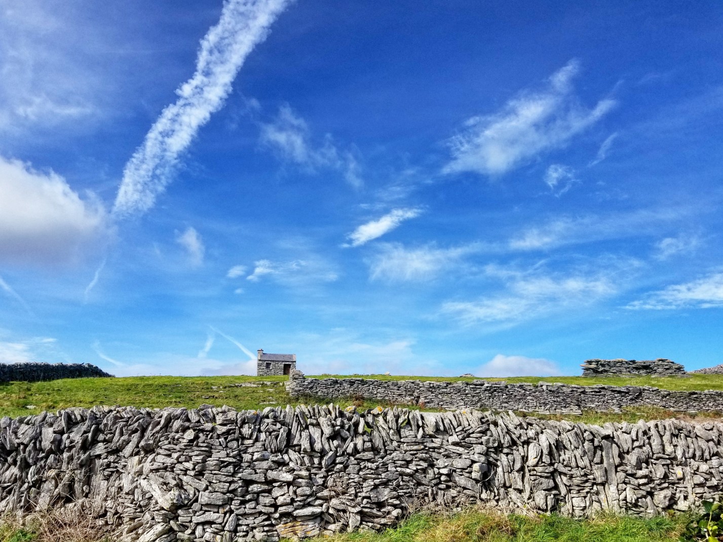 Stone wall on grassy field with blue skies during daytime