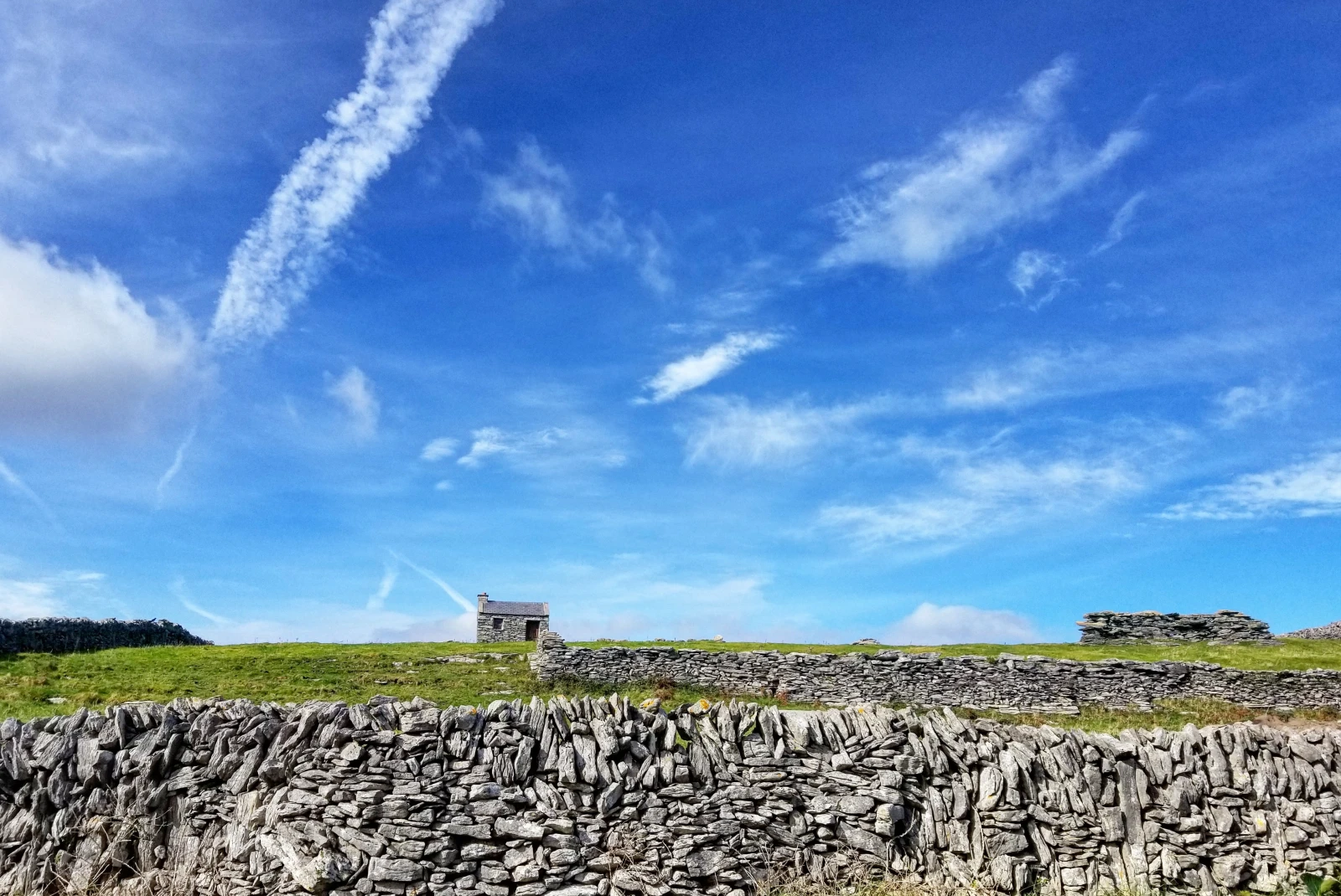 Stone wall on grassy field with blue skies during daytime