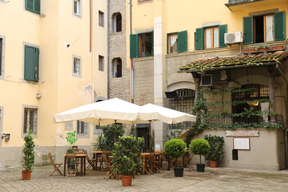 outdoor restaurant with white umbrellas, potted green plants and wood tables behind cream building with green shutters