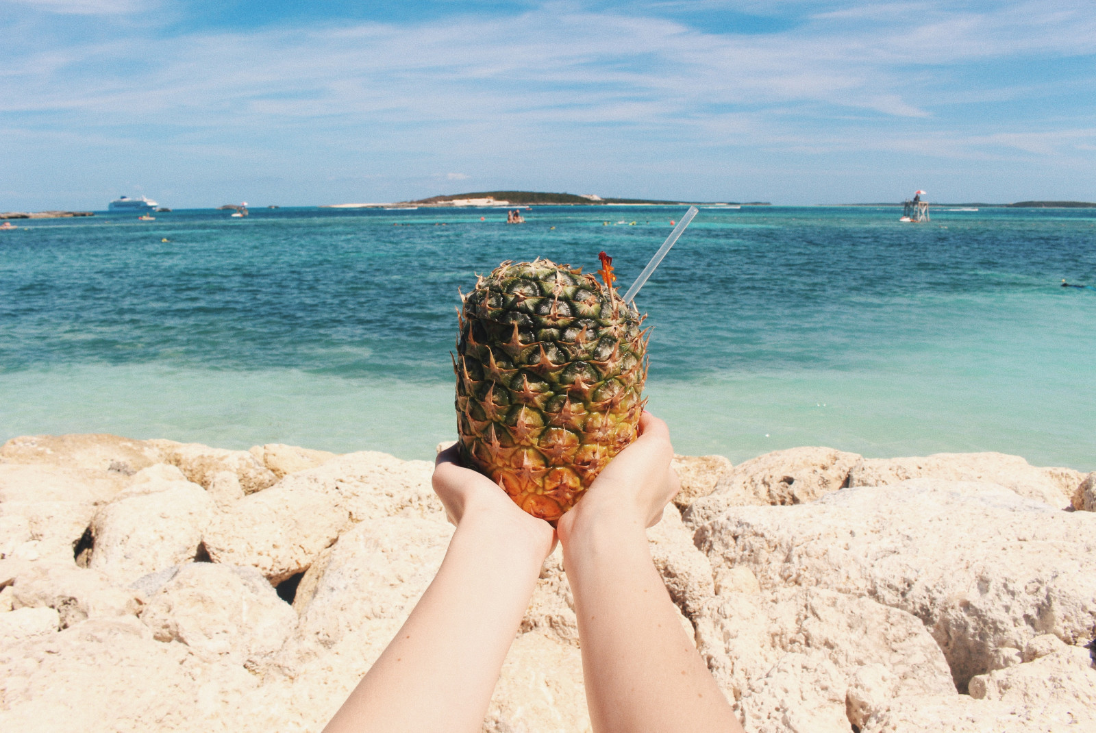 A person holding a pineapple drink/cocktail in from of the ocean in CocoCay, Bahamas