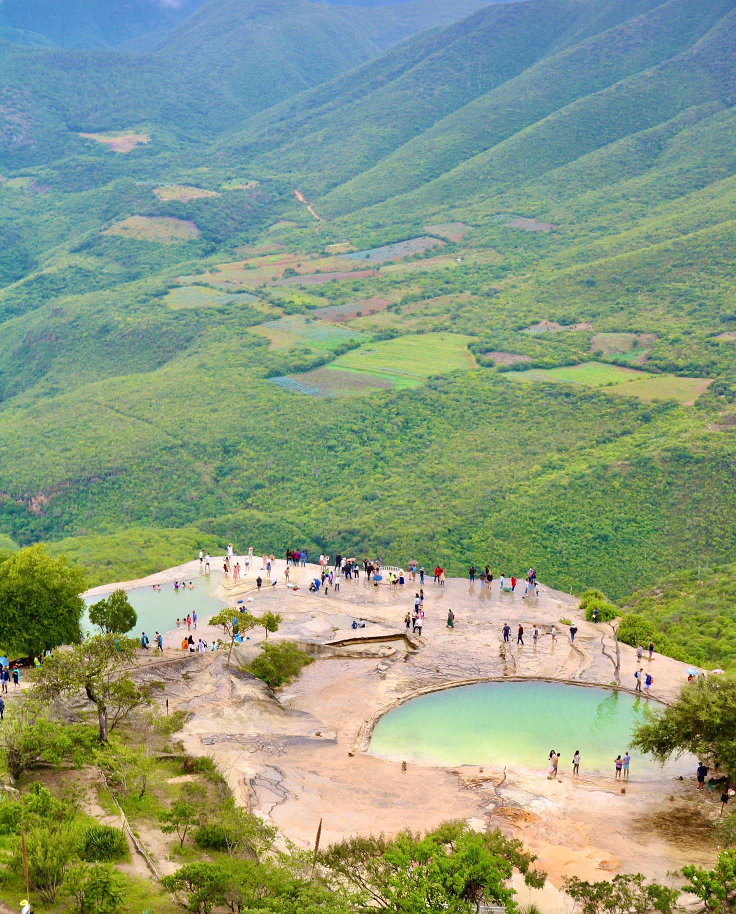 aerial view of people standing near pools of water surrounded by mountains