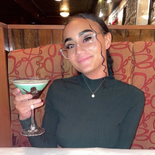 Travel Advisor Indyca Hassell sitting at a restaurant in black turtle neck with a cocktail. 