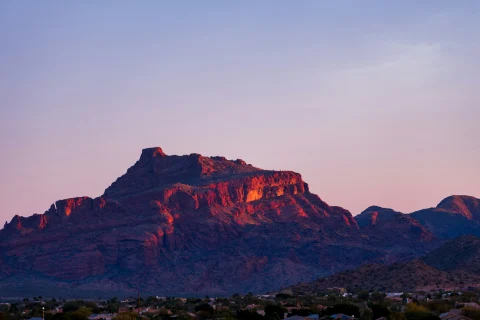 A large natural mesa in the distance with a town in the foreground at sunrise.
