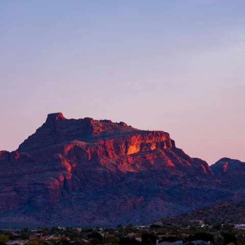 A large natural mesa in the distance with a town in the foreground at sunrise.