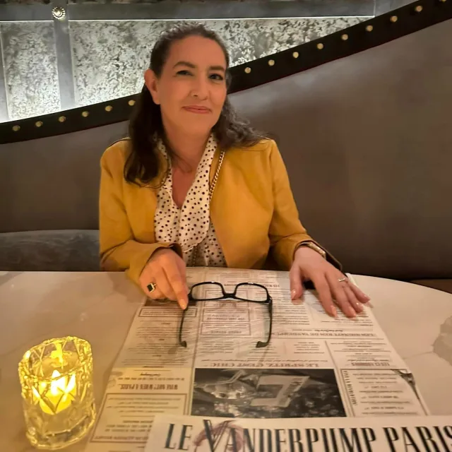 Picture of Melinda in yellow coat seated at a dining room table