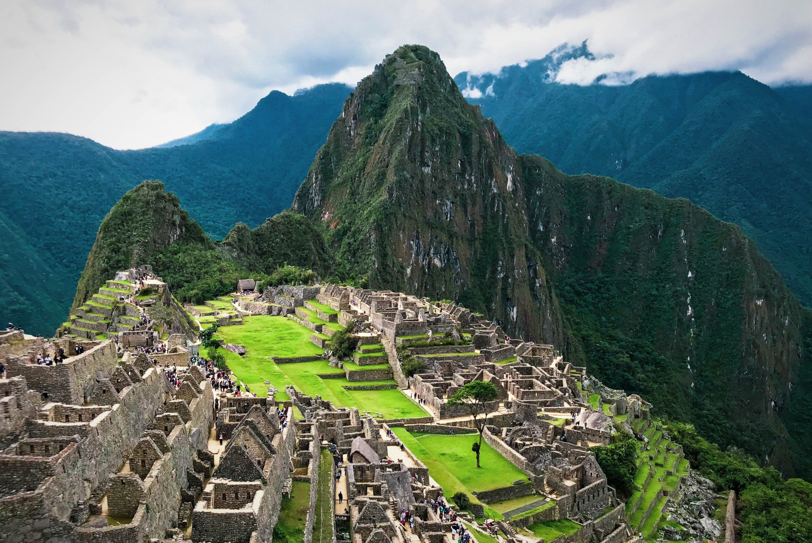machu picchu peru overview of grey ruins with green grass and tall rocky mountains and white clouds