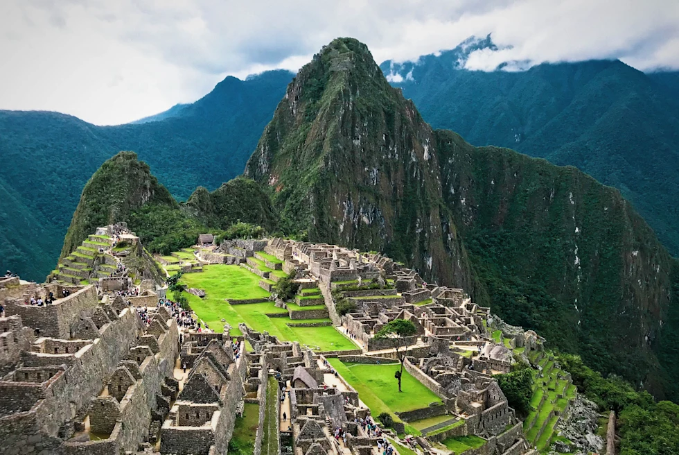 machu picchu peru overview of grey ruins with green grass and tall rocky mountains and white clouds