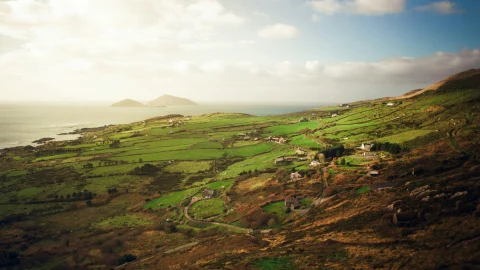 An aerial view of the green Irish landscape and sea on a golden-sunny day.
