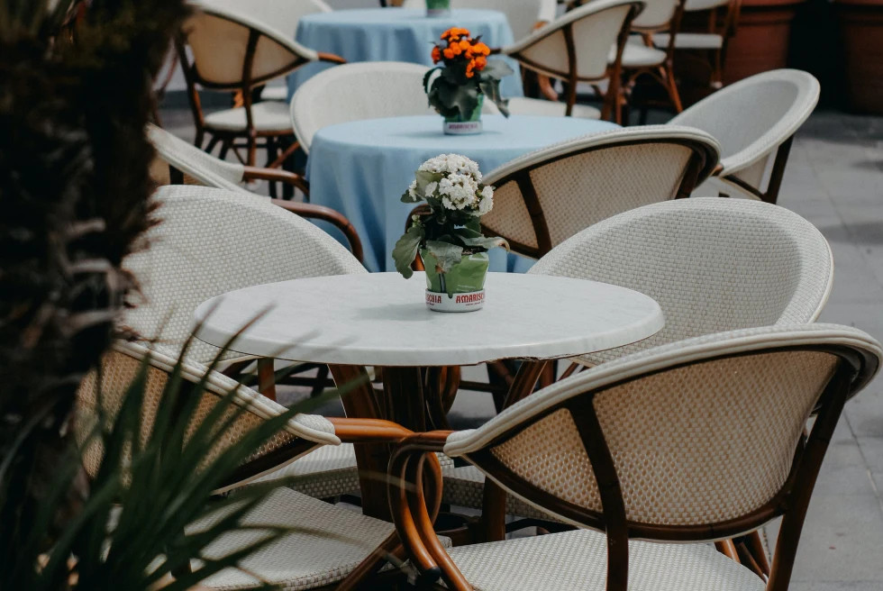 Outdoors seating with tables and chair and vases with flowers. 