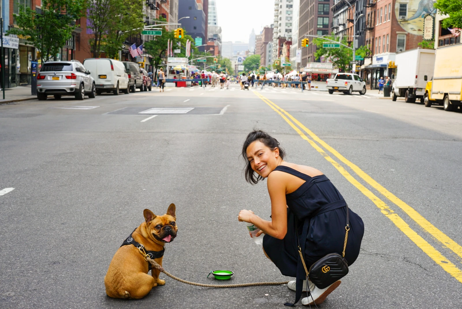 Dog and woman stand in street in NYC with buildings in background