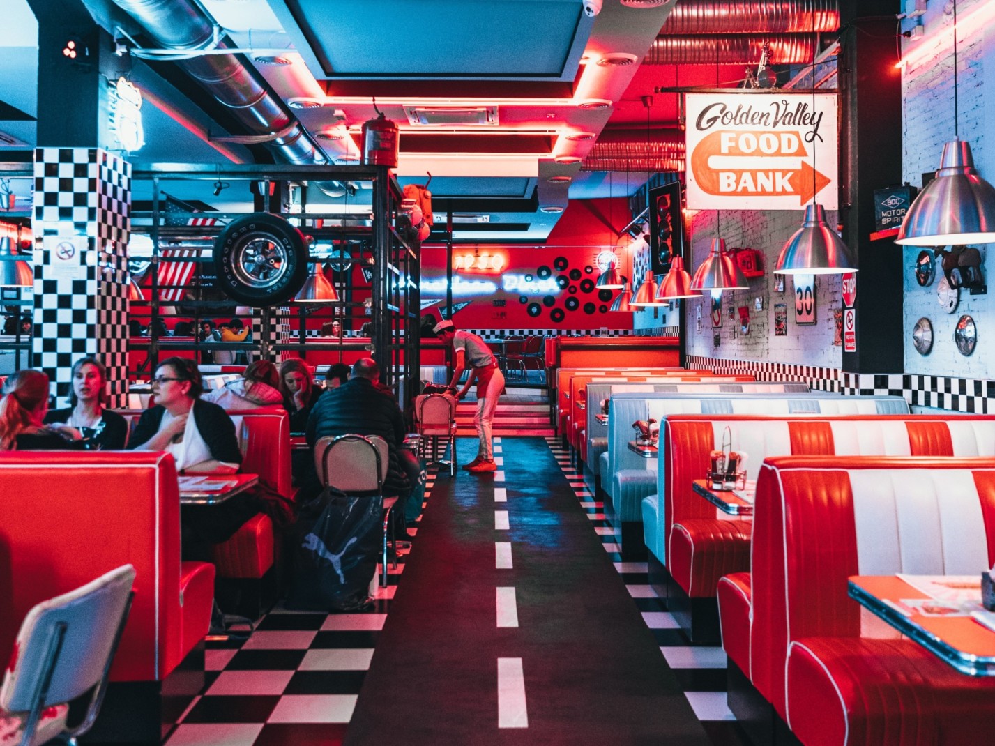 Retro diner with red and white leather booths, checkered tiles and neon lighting. 