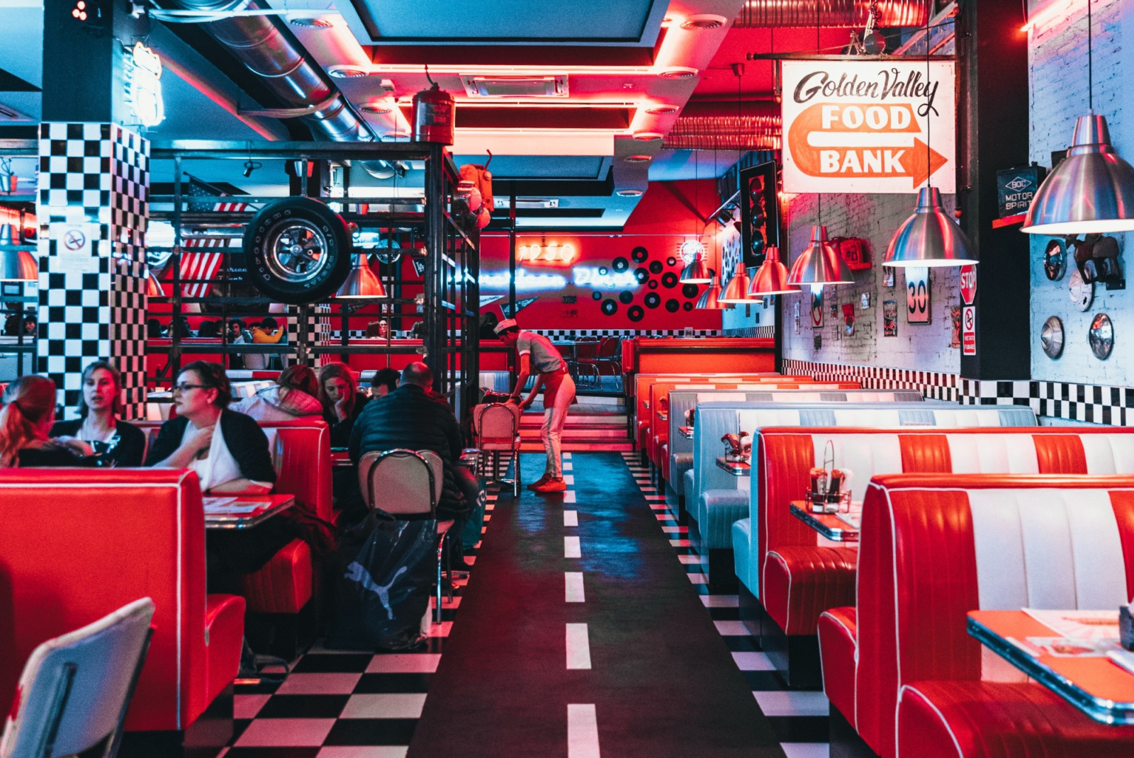 Retro diner with red and white leather booths, checkered tiles and neon lighting. 