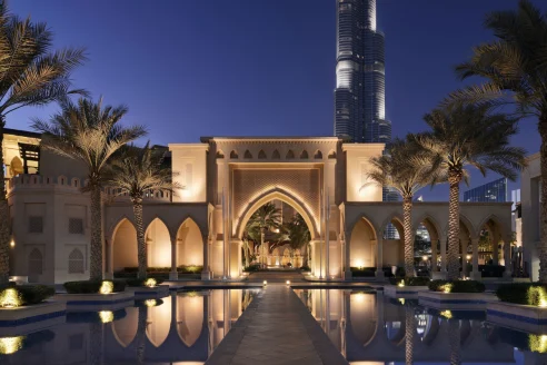 Middle Eastern courtyard with a reflective pool leading up to an illuminated tan archway