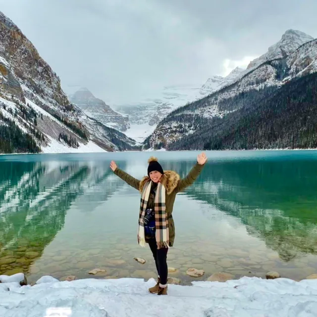 Travel Advisor Kalli Ziangos standing on snow in front of mountains and a blue lake.