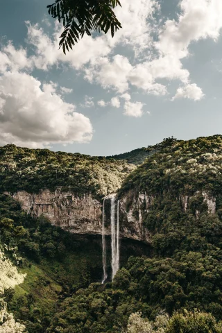 A waterfall in Brazil flowing off a large rocky mountain with lush green forest.