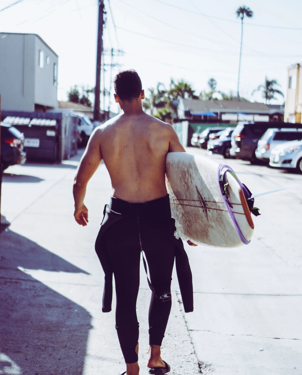 surfer walks with his surfboard down street