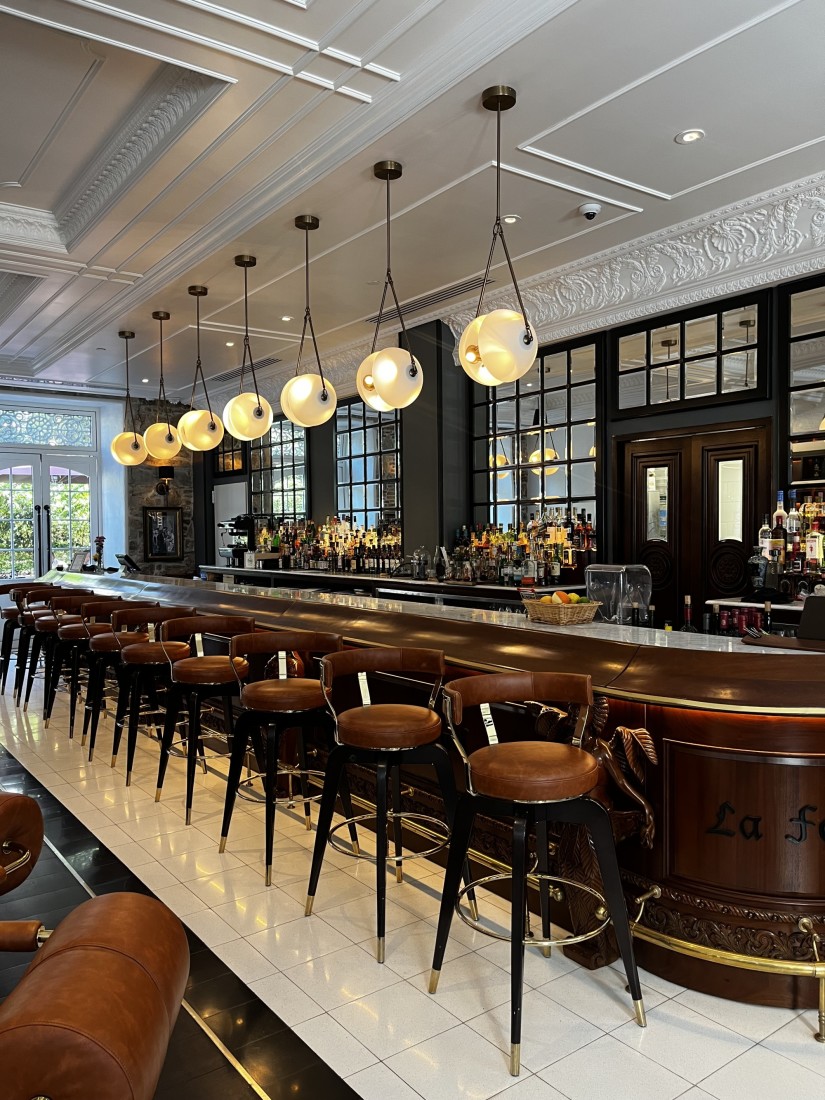 A beautiful bar with leather stools, white tiled flooring, hanging pendant lighting and white detailed ceilings. 