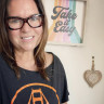 Fora Travel Agent Christine Armand wearing glasses and orange and black shirt standing in front of colorful art piece