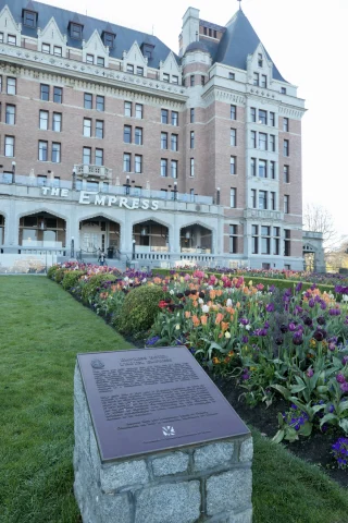 A historic plaque and landscaped flowerbeds in front of the Empress Hotel