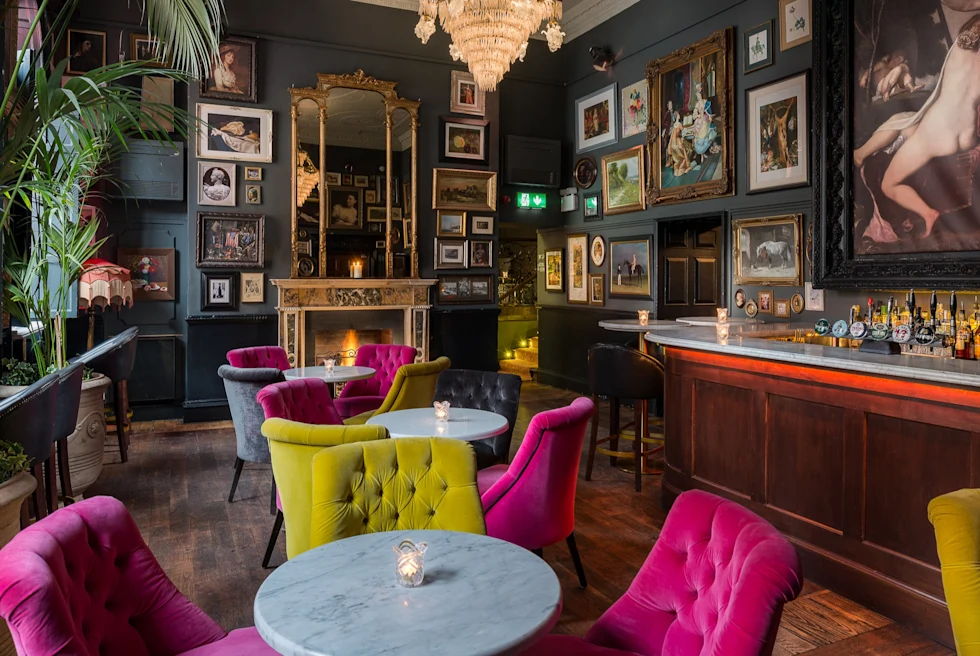 A restaurant with pink and yellow sofa chairs and round white tables.