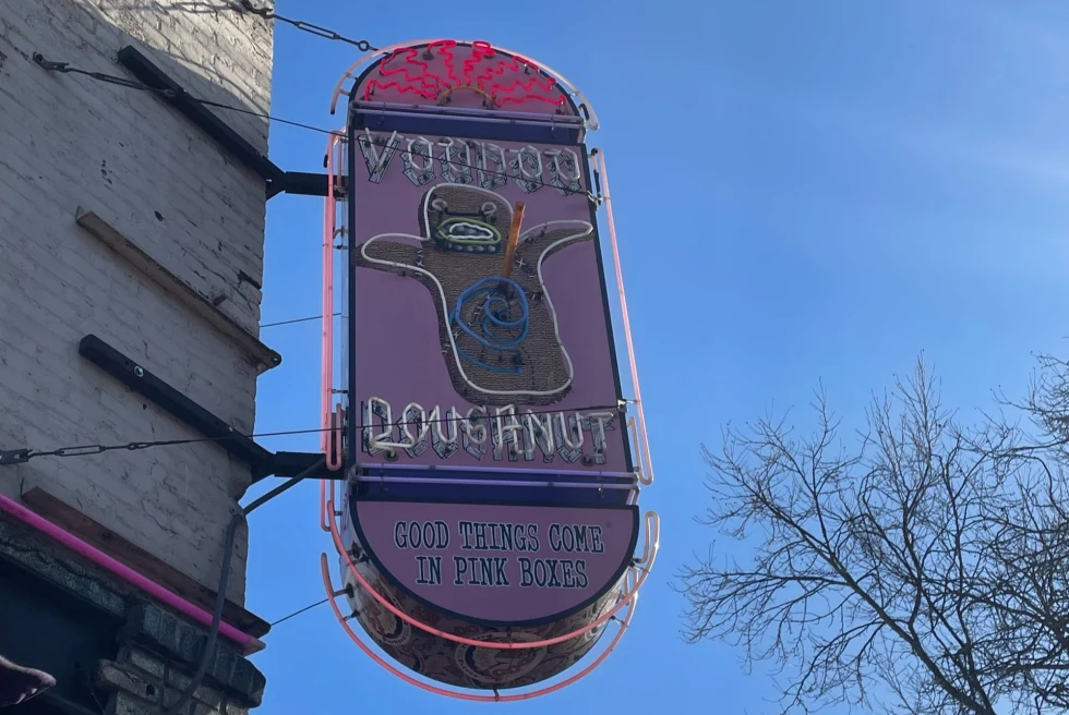 pink neon sign reads, "voodoo donuts" with a spooky ghost like cartoon