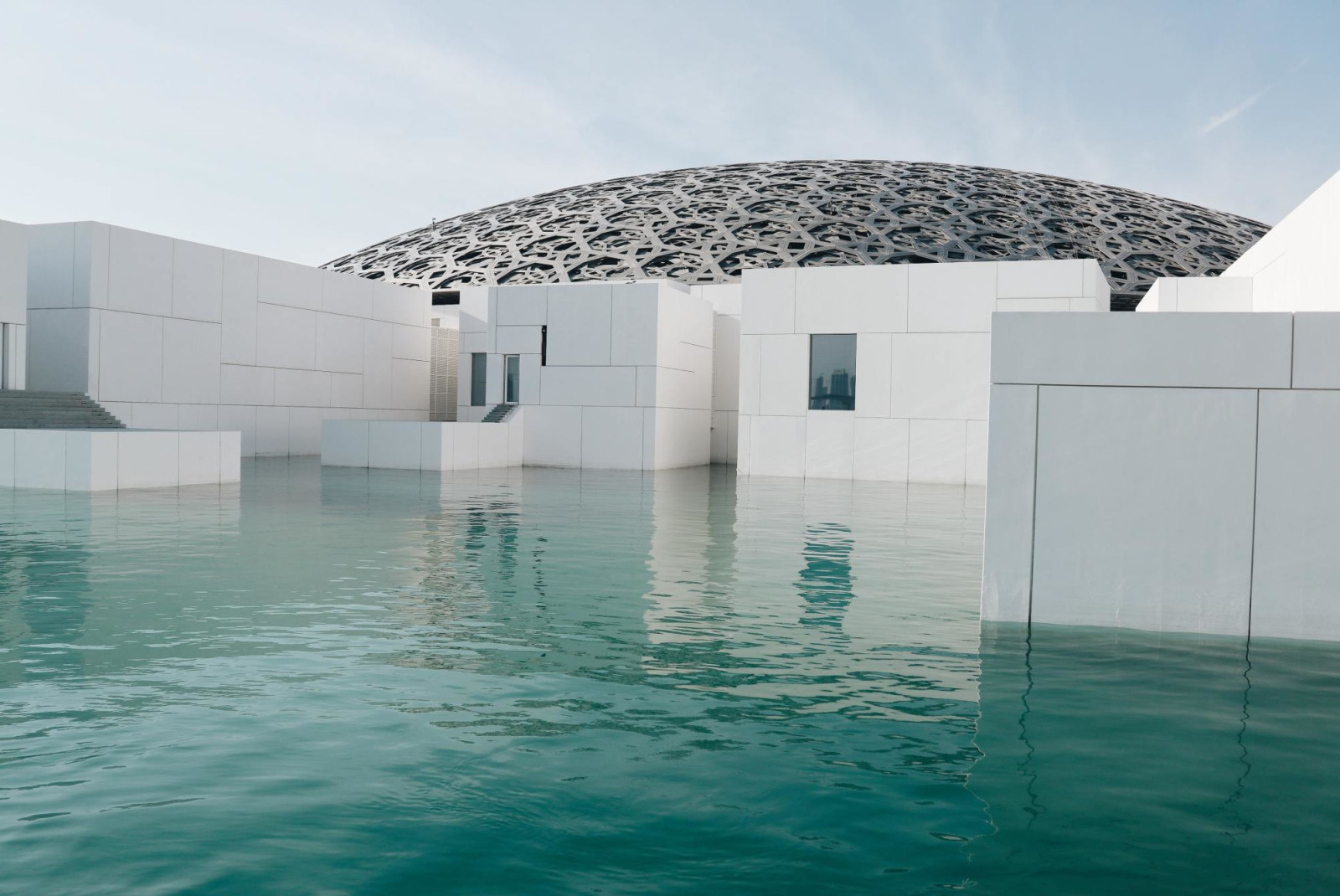 Modern white buildings and circular dome in Louvre Abu Dhabi on a sunny day.